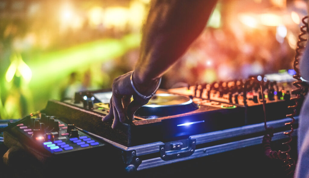 Dj mixing outdoor at beach party festival with crowd of people in background - Summer nightlife view of disco club outside - Soft focus on hand fingers - Fun ,youth,entertainment and fest concept