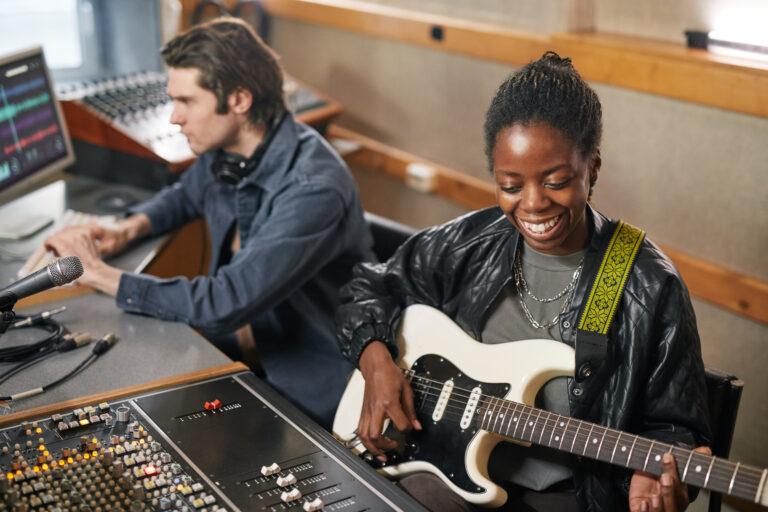 Portrait of smiling black woman playing guitar while producing music in professional recording studio